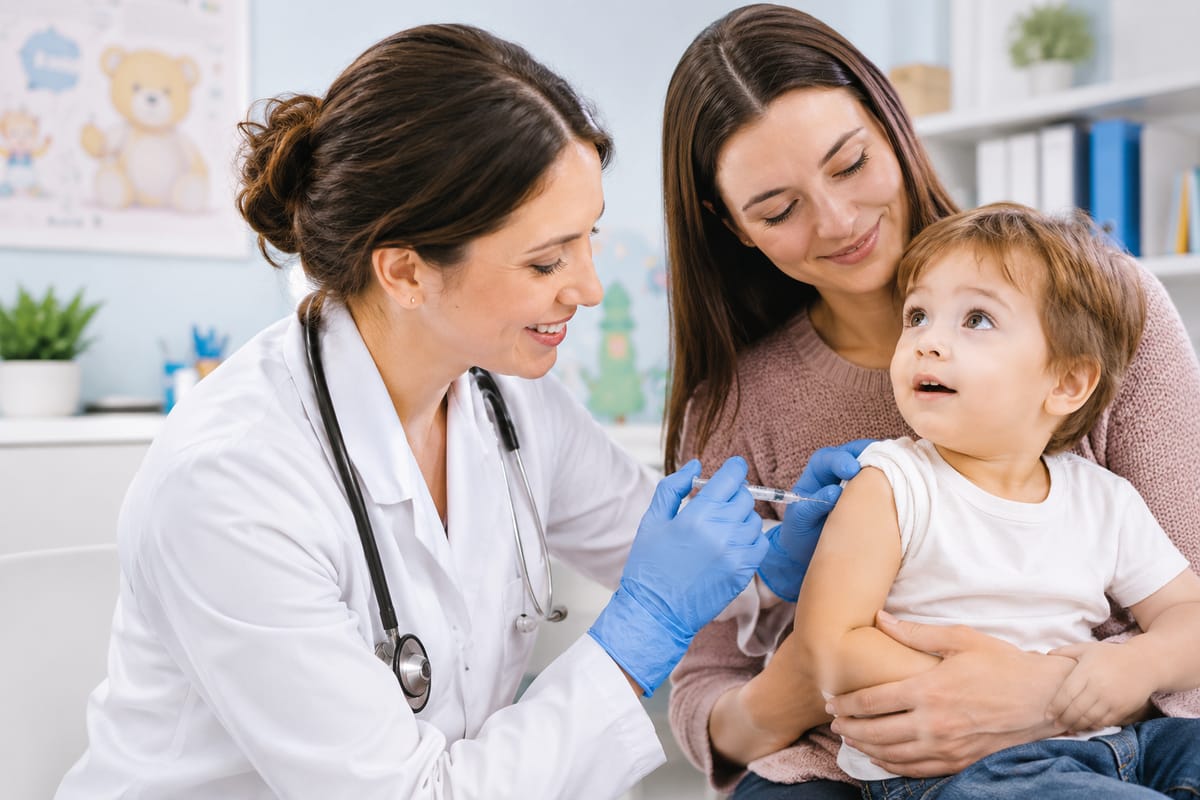 Medic vaccinând un copil mic, ținut în brațe de mama lui, în cabinet